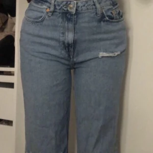 Jeans - Blåa jeans med hål vid ena benet, bra skick och längden är till fotknölarna 