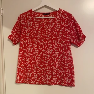 Röd blus - Röd blus med vita blommor, lite rynkad ärm och V ringad. Super fin sommartopp!! 