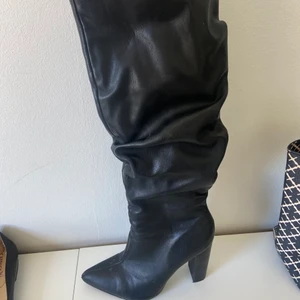 Höga stövlar - Höga svarta stövlar från Public Desire, modellen är ”skrynklig” längstmed vaden. Klackhöjd 10 cm. Stövlarna går upp till knät. 