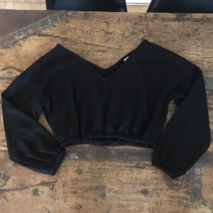Croppad sweater NLY trend - Svart croppad sweater med V-ringning och elastisk midja samt ärmslut. Använd 1 gång. Stl M.