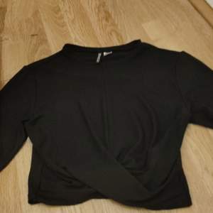 En långärmad svart tröja med ett kryss vid magen typ