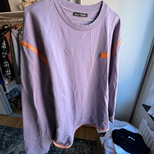 Acne Studios - Lila/grön/orange tröja i herrmodell. Grönt prassligt material på underarmen.