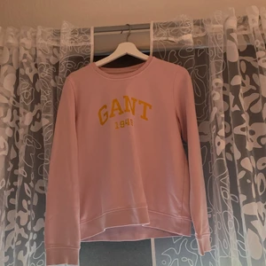 En super fin Gant sweetshirt i färgen rosa  - Säljer en super fin Gant sweetshirt med guldig text. Super fin och kan användas till sena sommarkvällar. Den har ett hål men inget man kan se.