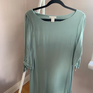 Grönturkos klänning med öppen ärm - 👗 Grönturkos klänning med öppen trekvartsärm med knyten från H&M, storlek 36. Skick utan anmärkningar utöver att den är skrynklig nu efter för lång tid nedpackad. SKICKAS med postnords fraktpåse för 63kr, önskas spårbart tillkommer det.