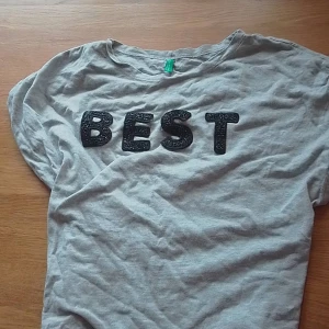 Grå t shirt -  Det här är en väldigt simpell grå t shirt, den är bekväm och fin. Det står "best" i svart glitter, den är s men den är väldigt stretchig.