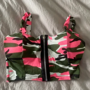Perfekt för halloween  - Militärmönstrad croppad topp med rosa inslag. Endast testad. Står ingen storlek med uppskattar den som small. Ganska tunt tyg vilket gör att padsen syns lite igenom när man har på sig toppen. Men kul för halloween eller någon temafest