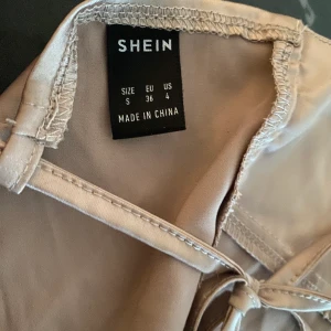 Beige festtopp i glatt tunt material från Shein. Strl. S/36 - Beige festtopp i glatt material från Shein. Storlek S, funkar även för XS eftersom man kan justera storlek i ryggen. Endast provad. Köparen står för frakt🌻
