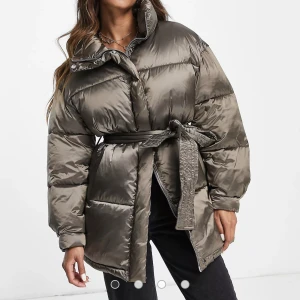 Dunjacka/pufferjacka - Dunjacka i en grönbrun färg med glansigt material. Väldigt varm. Den är oversize i storleken och i väldigt fint skick. Löstagbart skärp. Inköpspris 1200kr.