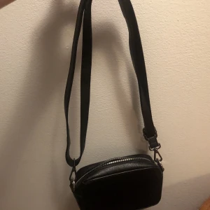 Svart axelremsväska  - En liten svart axelremsväska. Den är använd några gånger men kommer inte till användning.