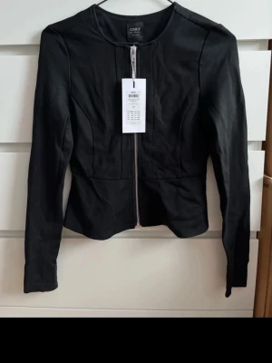 Svart cardiganjacka från ONLY - Snygg svart cardiganjacka från ONLY med dragkedja framtill och figurnära passform. Jackan har rund halsringning och långa ärmar. Perfekt för att lyfta din outfit med en stilren touch.