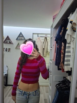 Rosa och röd cropped randig tröja - Säljer en tight, långärmad cropped tröja med ränder i rosa och rött. Tröjan har rund halsringning och är gjord i ett stretchigt, mjukt material som sitter snyggt på kroppen. Perfekt för dig som gillar färg och vill sticka ut. Använd ändast nån gång.