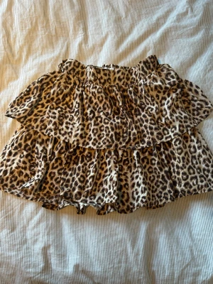 Leopardmönstrad volangkjol  - Säljer en kort kjol från Name It med leopardmönster och dubbla volanger. Kjolen har elastisk midja och är i mjukt, lätt material som ger en skön känsla. Perfekt att ha med ett vitt linne en sommardag! 