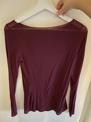 Vinröd långärmad topp Intimissimi - Säljer en vinröd långärmad topp från Intimissimi. Toppen är tunn och stretchig med en enkel, stilren design och rund halsringning. Perfekt att styla lager på lager eller bära som den är. Materialet känns mjukt och följsamt mot huden.