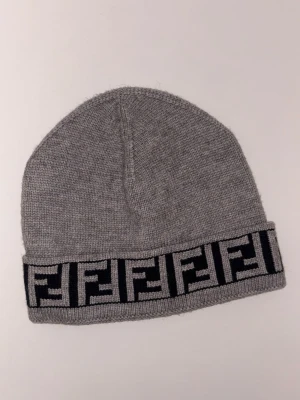 Fendi mössa – grå med FF logo 🧢 - Grå stickad mössa från Fendi med ikoniskt FF-mönster runt kanten. Tidlös och stilren design som passar till allt, perfekt för kalla dagar. Mjuk, varm och i fint skick – redo för en ny ägare! 🧢