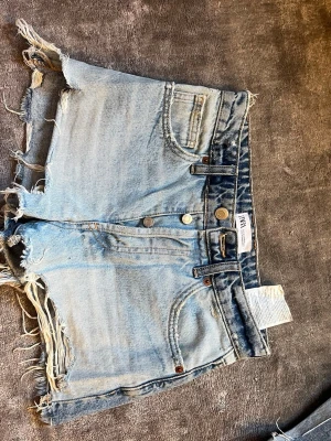 Ljusa denimshorts från Zara - Säljer ett par ljusa denimshorts från Zara med råa, fransiga kanter och klassisk femficksdesign. Shortsen har slitna detaljer som ger en cool och avslappnad look. Perfekta för varma dagar och enkel att matcha med t-shirt eller linne.
