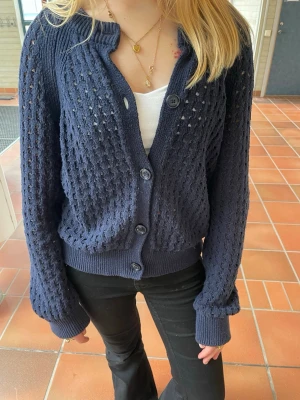 Mörkblå stickad kofta med knappar - PRIS KAN DISKUTERAS!                         Snygg mörkblå stickad kofta med hålmönster och stora knappar framtill. Koftan har ribbade muddar vid ärmslut och nederkant samt en avslappnad passform. Perfekt att slänga över en topp för en chill look.