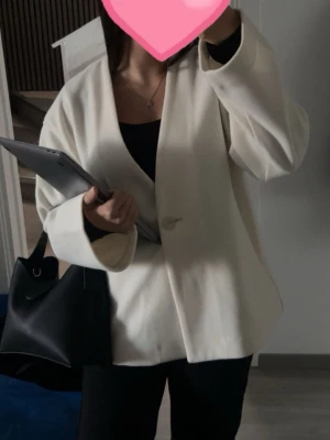 Oversized vit kavaj med enkel knapp - Stilren oversized vit kavaj med en knapp framtill och breda slag. Kavajen har en rak passform och är tillverkad i ett slätt tyg som ger en clean look. Perfekt att styla med svarta byxor och accessoarer för en modern outfit.