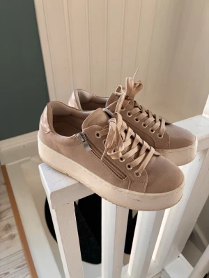 Beige platåsneakers från So All - Snygga beige sneakers från So All med platåsula och dragkedja på sidan. Skorna har klassisk snörning och är tillverkade i textilmaterial med matchande beige sula. Perfekta för dig som vill ha lite extra höjd och en clean look.