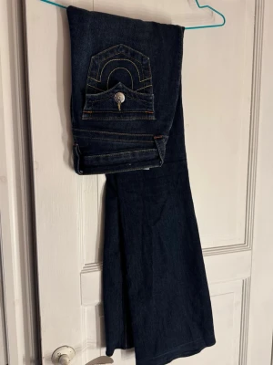 Bootcut jeans från True Religion - Säljer ett par mörkblå bootcut jeans från True Religion med snygga kontrastsömmar och ikonisk fickdetalj bak. Jag har sytt ned byxbenen (se bild 5) men det är något som inte syns vid användning. Relativt sparsamt använda.