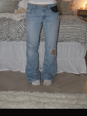Levi's ljusblå bootcut jeans - Säljer ett par ljusblå Levi's jeans med bootcut passform och slitning på ena benet. Klassisk femficksmodell med Levi's logga på bakfickan och knappgylf. Jeansen har en avslappnad vibe och är tillverkade i bomull.