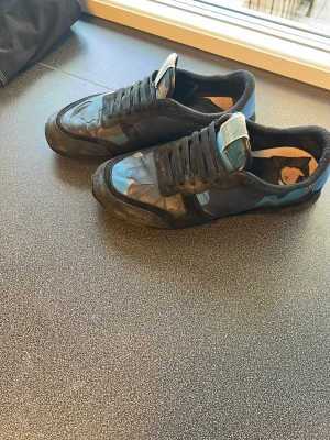 Valentino rockrunners - Snygga svarta sneakers från Valentino med blå och grå camo-detaljer. Skorna har låga skaft, svarta snören och en beige patch med logga på plösen. Tillverkade i en mix av läder och textil för en cool och unik look. Pris går att diskutera vid snabb affär!!!