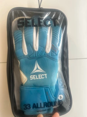 Blå målvaktshandske från Select - Snygg blå målvaktshandske från Select, modell 33 Allround. Handsken har vit och blå design med logga på ovansidan, negativ cut och bred kardborrestängning. Tillverkad i latex och mesh för bra grepp och komfort. Perfekt för både träning och match.
