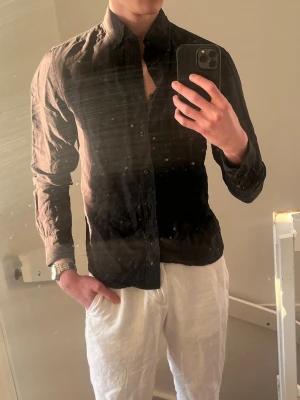 Svart skjorta från Bläck - Stilren svart skjorta med klassisk krage och knappar hela vägen framtill. Skjortan är långärmad och har en smal passform som ger en snygg siluett. Perfekt för dig som gillar en clean och enkel look.