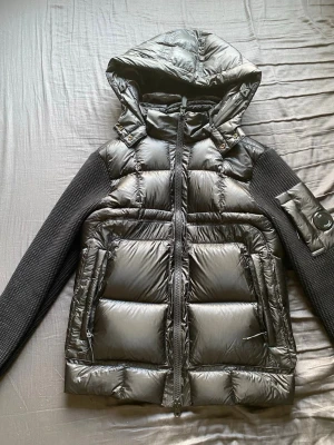 C.P Company cardigan - Snygg svart cardigan från C.P company med stickade ärmar och huva. Den har två framfickor med dragkedja och logga på ena ärmen. Kombinerar glansigt dunmaterial med stickad struktur för en modern look. Storlek S men kan passa XS. Skriv privat vid frågor!