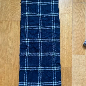 Mörkblå rutig halsduk - Snygg mörkblå halsduk med klassiskt rutmönster i vitt och grått. Halsduken är rektangulär och passar perfekt för att ge din outfit en stilren touch. Materialet känns mjukt och bekvämt mot huden. Perfekt accessoar för kyligare dagar.