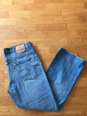 Blå Levi's 517 Bootcut  - Klassiska blå Levi's jeans i rak modell med hög midja. Jeansen har fem fickor, bälteshällor och den ikoniska röda Levi's-lappen på bakfickan. Tillverkade i slitstark denim som ger en tidlös look. Perfekta för dig som gillar vintage vibe och enkel stil.