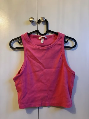 Rosa ribbad croppad linnetopp H&M - Säljer en rosa croppad linnetopp från H&M. Toppen är ribbad och ärmlös med en rund halsringning. Perfekt för varma dagar och enkel att matcha med jeans eller kjol.