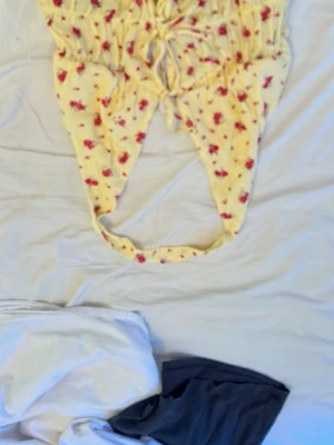 Gul sommar topp med blommönster - Söt gul baddräkt med små röda blommor och rynkade detaljer framtill. Baddräkten har smala axelband och knytning i midjan för en justerbar passform. Perfekt för strandhäng eller poolparty.