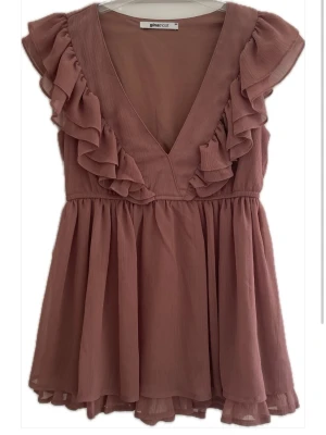 Rosa volangblus från Gina Tricot - Supersöt rosa blus från Gina Tricot med v-ringning och volangdetaljer längs axlar och bröst. Den har två små, små hål fram men verkligen inget man lägger till.