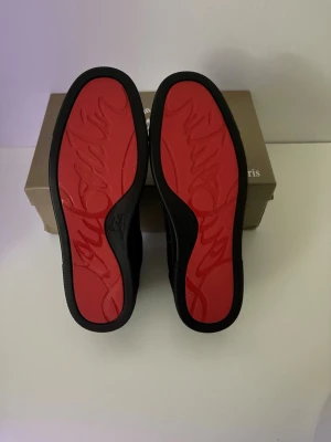 Svarta sneakers från Christian Louboutin - Snygga svarta sneakers från Christian Louboutin med klassiska röda sulor och diskret logga. Skorna är låga och har en ovandel i mocka och läderdetaljer. Perfekta för dig som vill ha en exklusiv och stilren look.