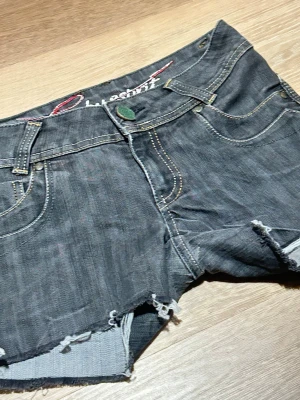 Svarta jeansshorts - Säljer ett par svarta jeansshorts, med fransiga kanter och klassisk femficksdesign. Shortsen har låg midja och slitna detaljer för en avslappnad look. Perfekta för sommardagar och festivaler.