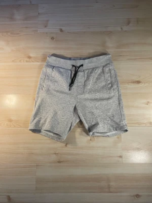Grå sweatshorts från Pier One - Grå mjuka sweatshorts från Pier One med snörning i midjan och två sidofickor. Perfekta för avslappnade dagar och har en klassisk, enkel design. Tillverkade i bomullsmix för extra komfort.
