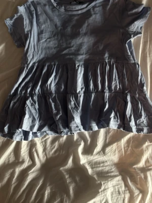 Ljusblå volangblus med kort ärm - Supersöt ljusblå blus med volanger och korta ärmar. Toppen har en avslappnad passform och rund halsringning. 