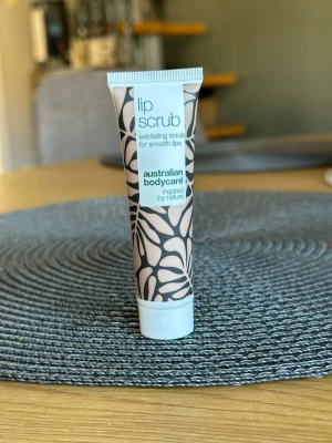 Lip scrub från Australian Bodycare - Exfolierande lip scrub i tub från Australian Bodycare. Tuben är beige med svart bladmönster och vit kork. Produkten är inspirerad av naturen och hjälper till att göra läpparna mjuka och släta.