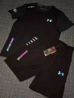 Svart set från Under Armour - Snyggt svart set från Under Armour med färgglada loggor och tryck. Setet består av en t-shirt och shorts, båda med UA-logga i regnbågsfärger. Perfekt för dig som gillar sportig och trendig stil.