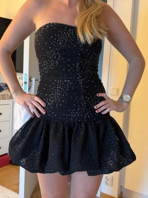Maje klänning - Maje roxanne noir, nypris 2700kr. Helt ny med prislapp! Supersnygg svart kort klänning från Maje med glittriga detaljer och voluminös kjol. Klänningen har en figurnära passform upptill och är täckt av små paljetter som ger en festlig look. Perfekt för dig som vill sticka ut!