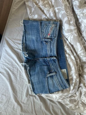 Blå lågmidjade jeansshorts från Diesel - Säljer ett par blå lågmidjade jeansshorts från Diesel med råa kanter och slitna detaljer. Shortsen har klassiska fem fickor, bälteshällor och en ljus tvätt. Perfekta för en avslappnad och cool stil. Pris går att diskutera 