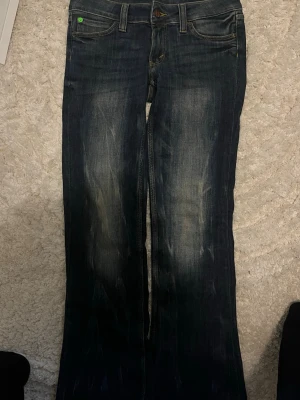 Mörkblå bootcut jeans från Cheap Monday - Snygga mörkblå bootcut jeans från Cheap Monday med slitningar framtill och klassiska fem fickor. Jeansen har en grön etikett bak och är tillverkade i denim med en cool tvätt. Perfekta för dig som gillar en avslappnad men trendig stil.