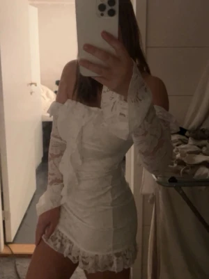 Vit spetsklänning offshoulder - Söt vit kortklänning i spets med offshoulder och långa ärmar. Klänningen har volangdetaljer vid halsringningen och nederkanten samt en liten rosett framtill. Perfekt för sommarens alla tillfällen. Även perfekt till studenten! Den är från Boohoo i storlek 36/S🩷🩷