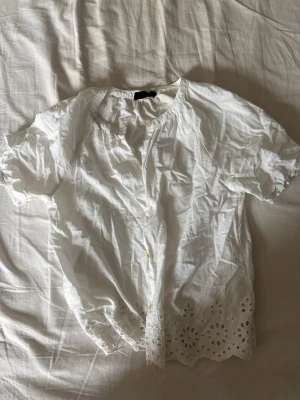 Vit blus med broderad kant Monoprix - Söt vit blus från Monoprix med korta ärmar. Perfekt nu till sommaren då den är gjord i ett tunt och luftigt material