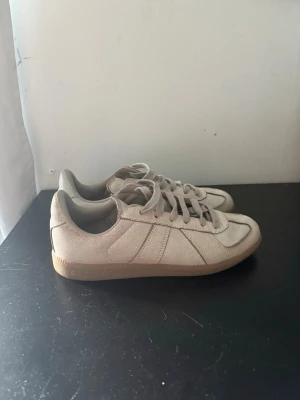 Beige gats från Adidas  - Snygga beige gats från Adidas i klassisk gummisula. Skorna har lågt skaft, tonade skosnören och diskret logga på plösen. Perfekta för en clean och cool look
