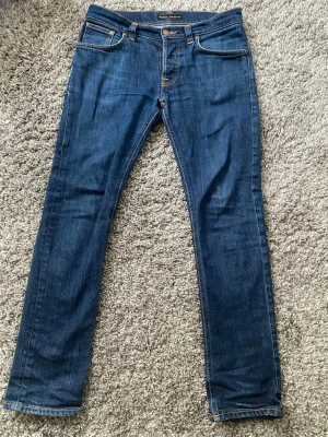 Nudie Jeans co - Ett par feta marinblå nudie jeans i väldigt bra skick, de är inte använda mycket och har inga skador. De är 39-40cm i midjan men har en del stretch i sig, längden på jeansen är 97cm, storleken är W31 L32.