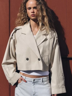 Kort beige trenchcoat med axelremmar - Trendig kort trenchcoat i beige med dubbelknäppning och markerade axelremmar. Jackan har bred krage, vida ärmar och är tillverkad i ett kraftigt tyg som ger en cool och avslappnad look. Perfekt att slänga över en t-shirt för en stilren outfit. Använt typ 2 ggr? Inga defekter💝