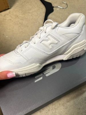 Vita New Balance 550 sneakers - Snygga vita New Balance 550 sneakers i läder med klassisk siluett och tydliga detaljer som perforeringar och den ikoniska N-loggan på sidan. Skorna har en chunky sula och lågt skaft, perfekta för en clean och sportig look.