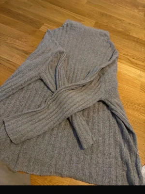 Grå ribbstickad kofta - Mysig grå kofta i ribbstickat material med långa ärmar och öppen front. Perfekt att slänga på sig över en t-shirt eller topp för en avslappnad look. Koftan har en mjuk känsla och är enkel att matcha med det mesta.