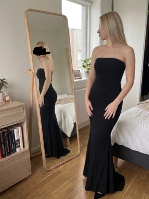 Balklänning  - Säljer en svart, elegant bandslös långklänning med figurnära passform och lätt utsvängd nederdel. Klänningen har bh stöd. Perfekt ifall man letar en balklänning.💕